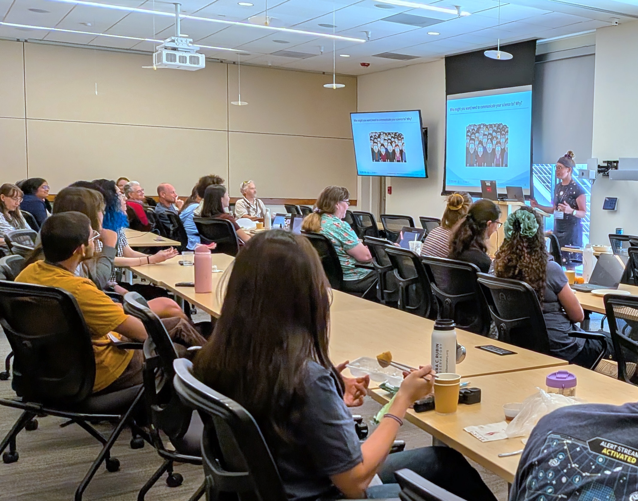 Stephanie speaking at the front of a room in front of a presentation screen